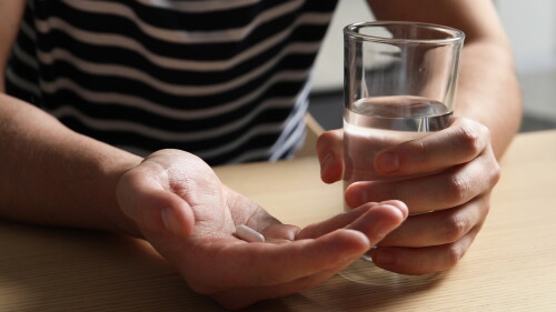 Man with glass of water and pill at wooden table, closeup