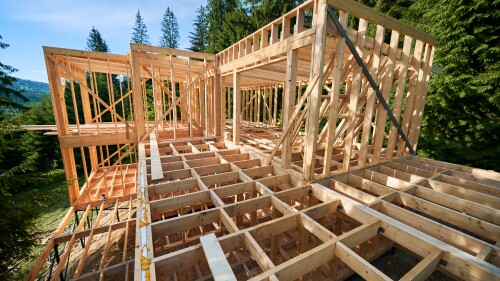 Wooden frame house under construction near forest.