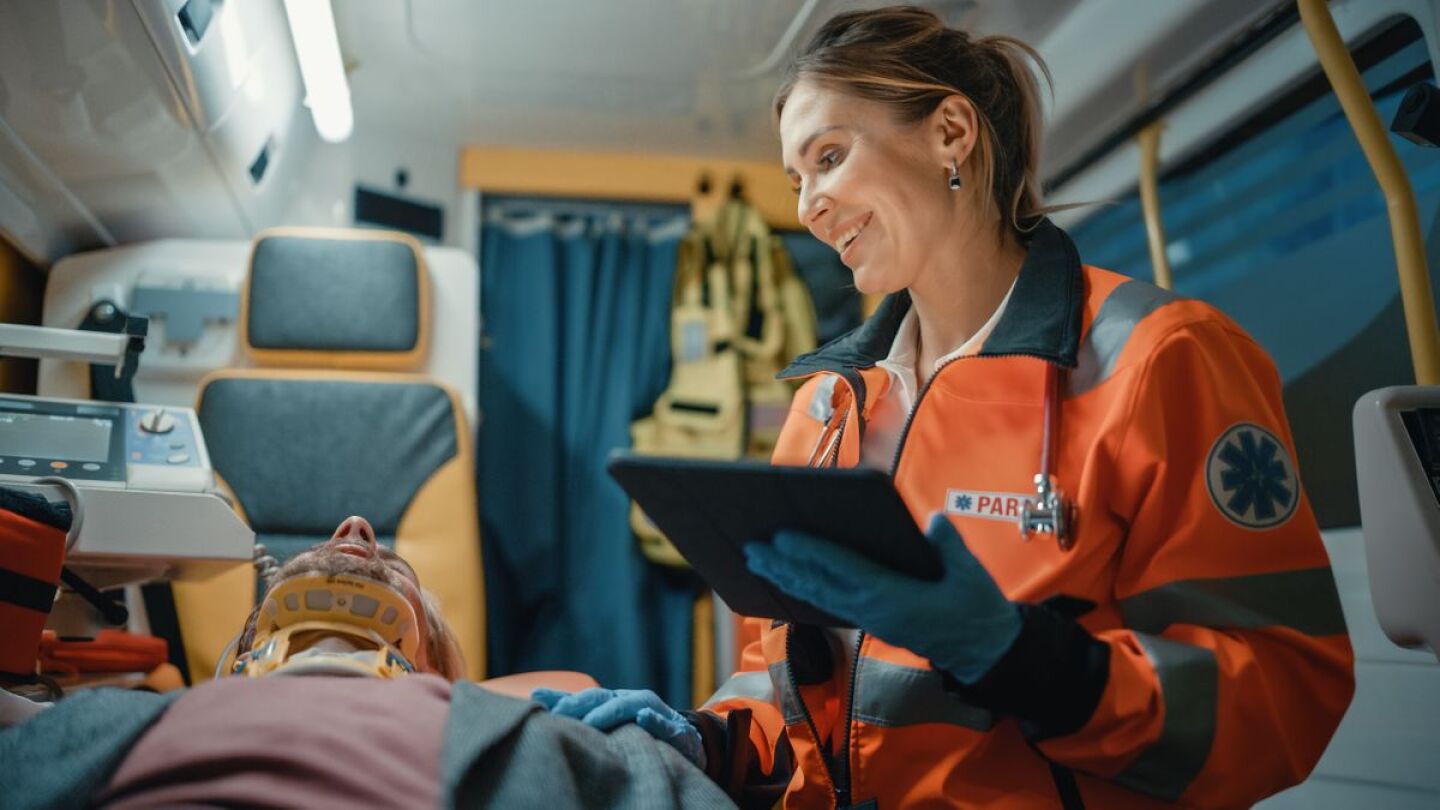 female paramedic with tablet smiling at prone patient in neck brace.jpg