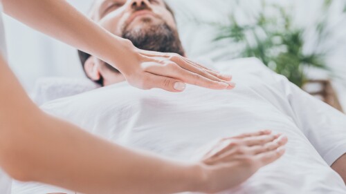 close-up view of bearded man receiving reiki healing session above stomach and chest