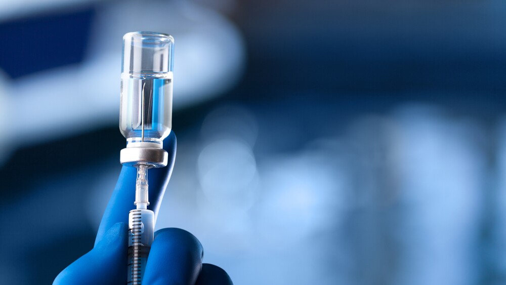 A medical hand in a glove holds an ampoule with a vaccine and a syringe with illustration