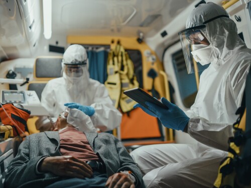 Paramedic in Coveralls Using Tablet Computer to Check the Diagnosis for the Injured Patient on the Way to Hospital. Emergency Medical Care Assistants Puts a Ventilation Mask in an Ambulance.