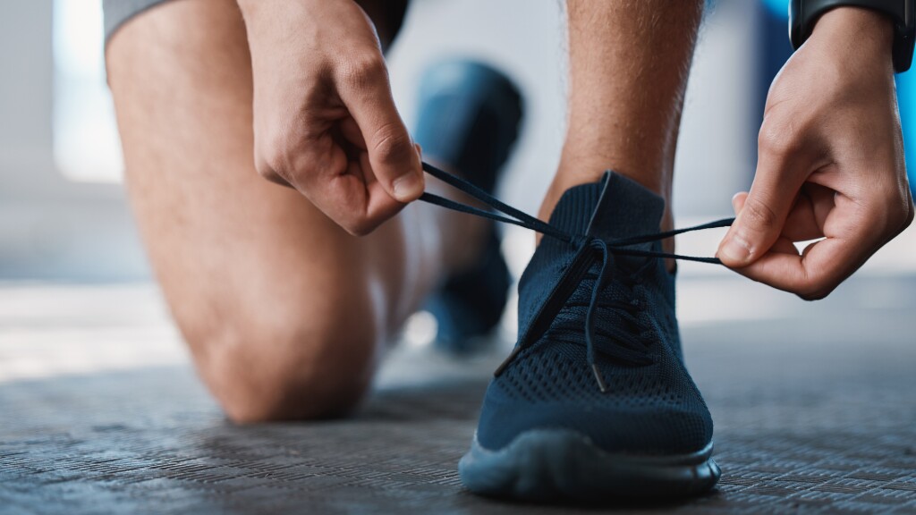 Fitness, shoes and tie with a sports man in the gym getting ready for a cardio or endurance workout. Exercise, running and preparation with laces of a male athlete or runner at the start of training