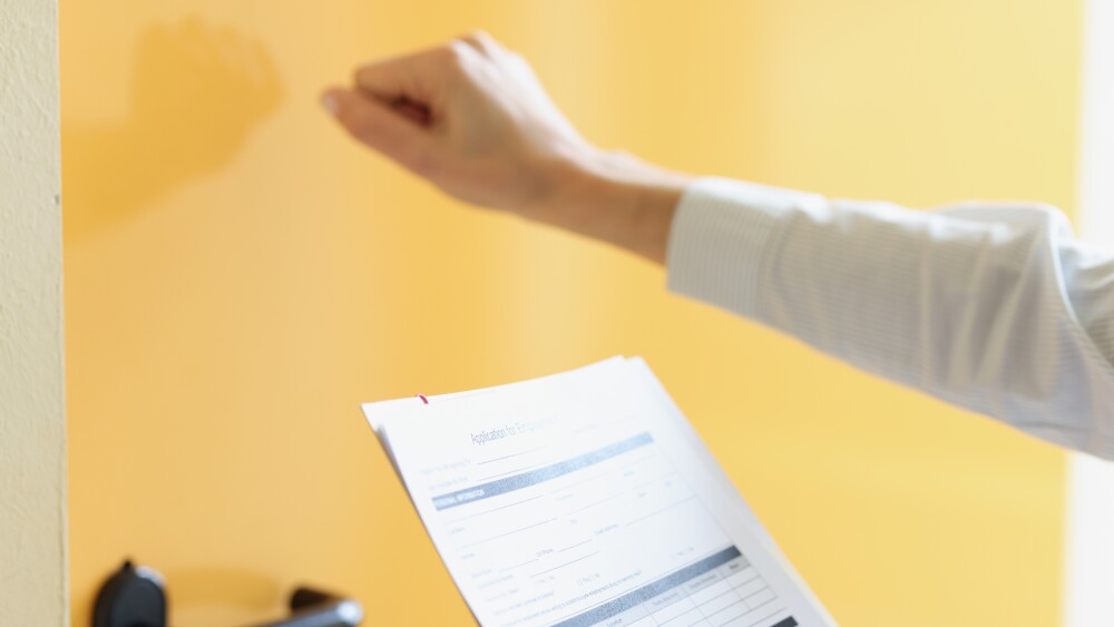 Woman holds application form in her hand and knocks on door